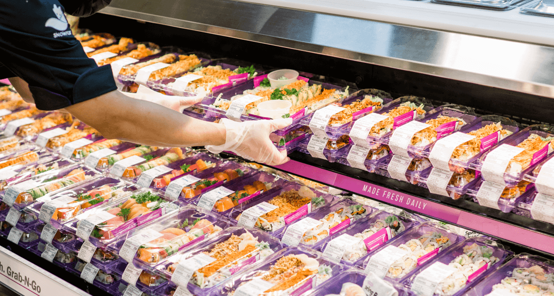 A worker placing sushi in a display area
